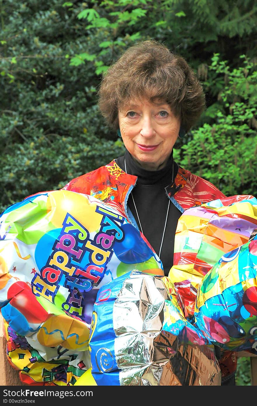 Mature female senior relaxing at home on her outdoor deck with happy birthday balloons.