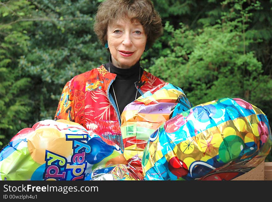 Mature female senior relaxing at home on her outdoor deck with happy birthday balloons.