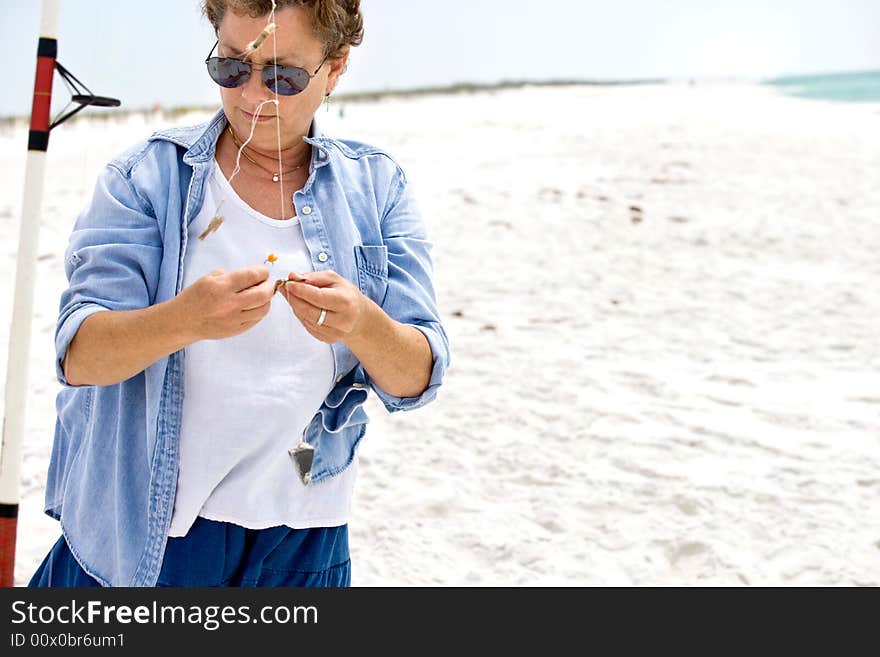 Mature woman baiting her fishing hooks at the beach; she's catching pompano!. Mature woman baiting her fishing hooks at the beach; she's catching pompano!