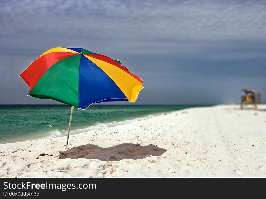 Colorful beach umbrella on a deserted beach as a storm approaches on the dark horizon. Colorful beach umbrella on a deserted beach as a storm approaches on the dark horizon