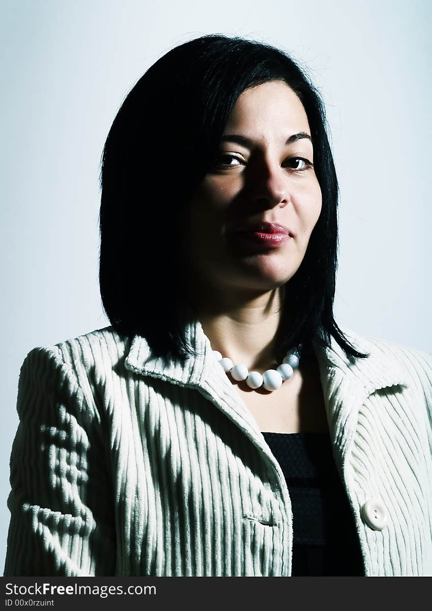 A high-key portrait about an attractive lady with black hair who is looking ahead, she is flirting and she has a charming look. She is wearing a white coat, a black dress, and a white necklace. A high-key portrait about an attractive lady with black hair who is looking ahead, she is flirting and she has a charming look. She is wearing a white coat, a black dress, and a white necklace.