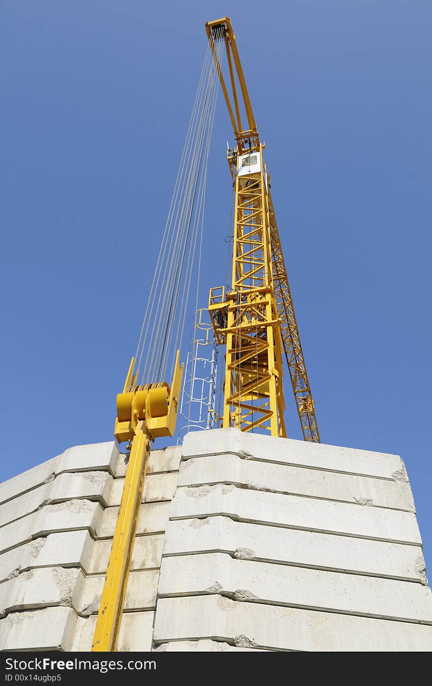 Tall yellow construction-crane with large counter-weights set against blue sky. Tall yellow construction-crane with large counter-weights set against blue sky