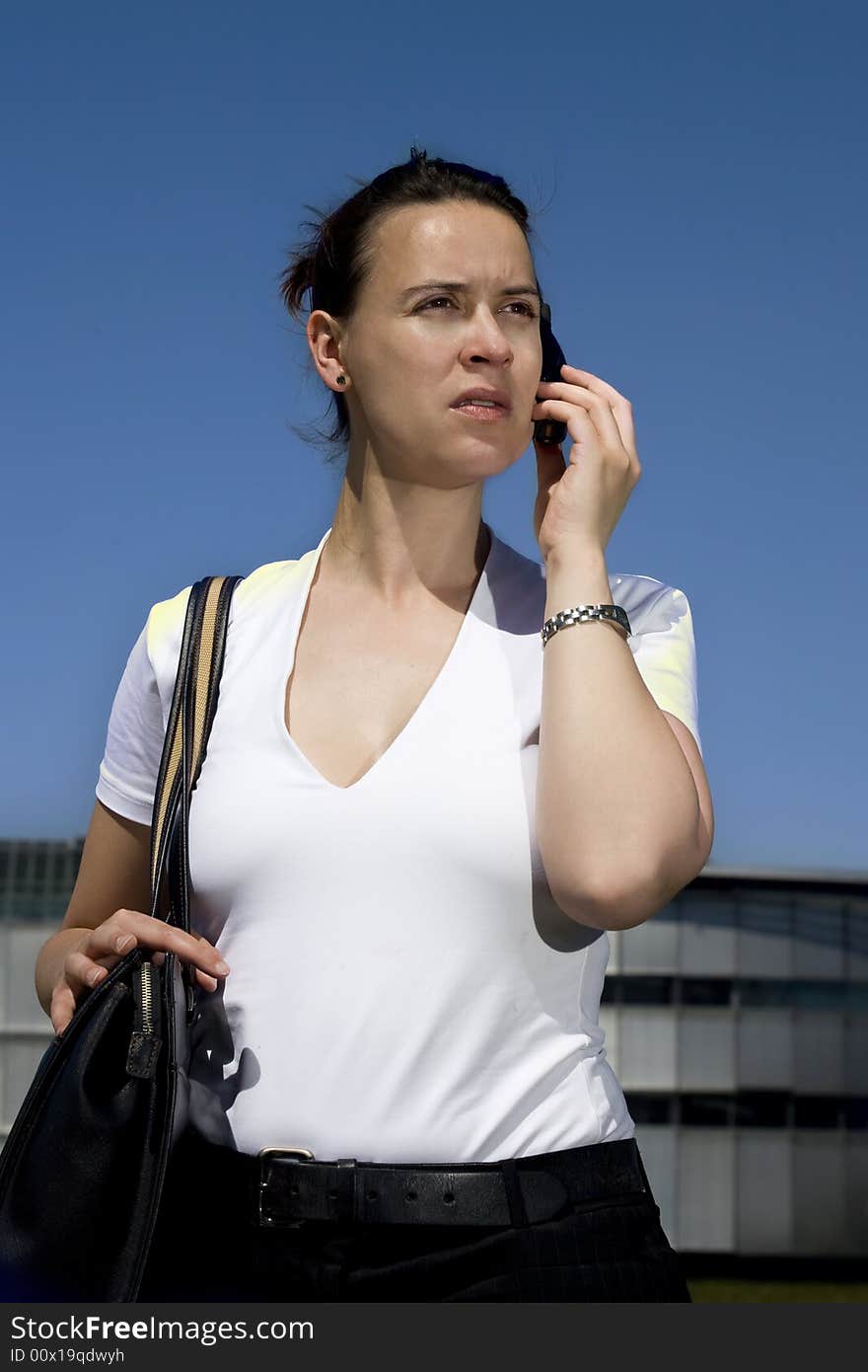 A woman calling on a cell phone in front of commercial buildings with blue sky. A woman calling on a cell phone in front of commercial buildings with blue sky