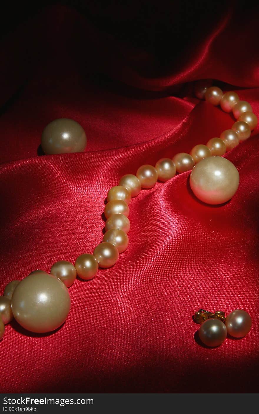 Pearl earrings and necklace on red silk background