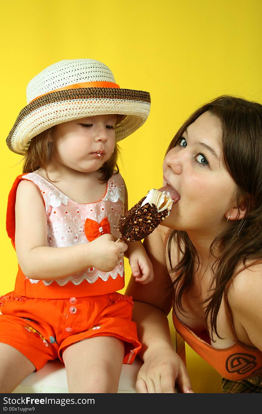 Two pretty sisters are eating ice-cream on yellow background. Two pretty sisters are eating ice-cream on yellow background