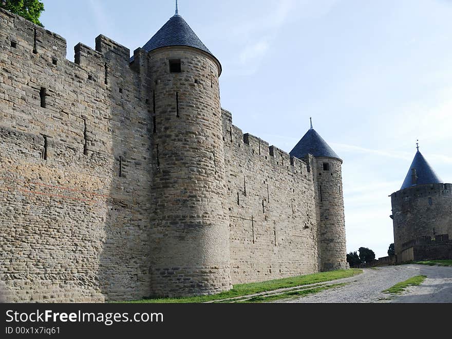 Inner old defense wall with conic towers of Carcasson castle in sunlight against blue sky and road along, France. Inner old defense wall with conic towers of Carcasson castle in sunlight against blue sky and road along, France