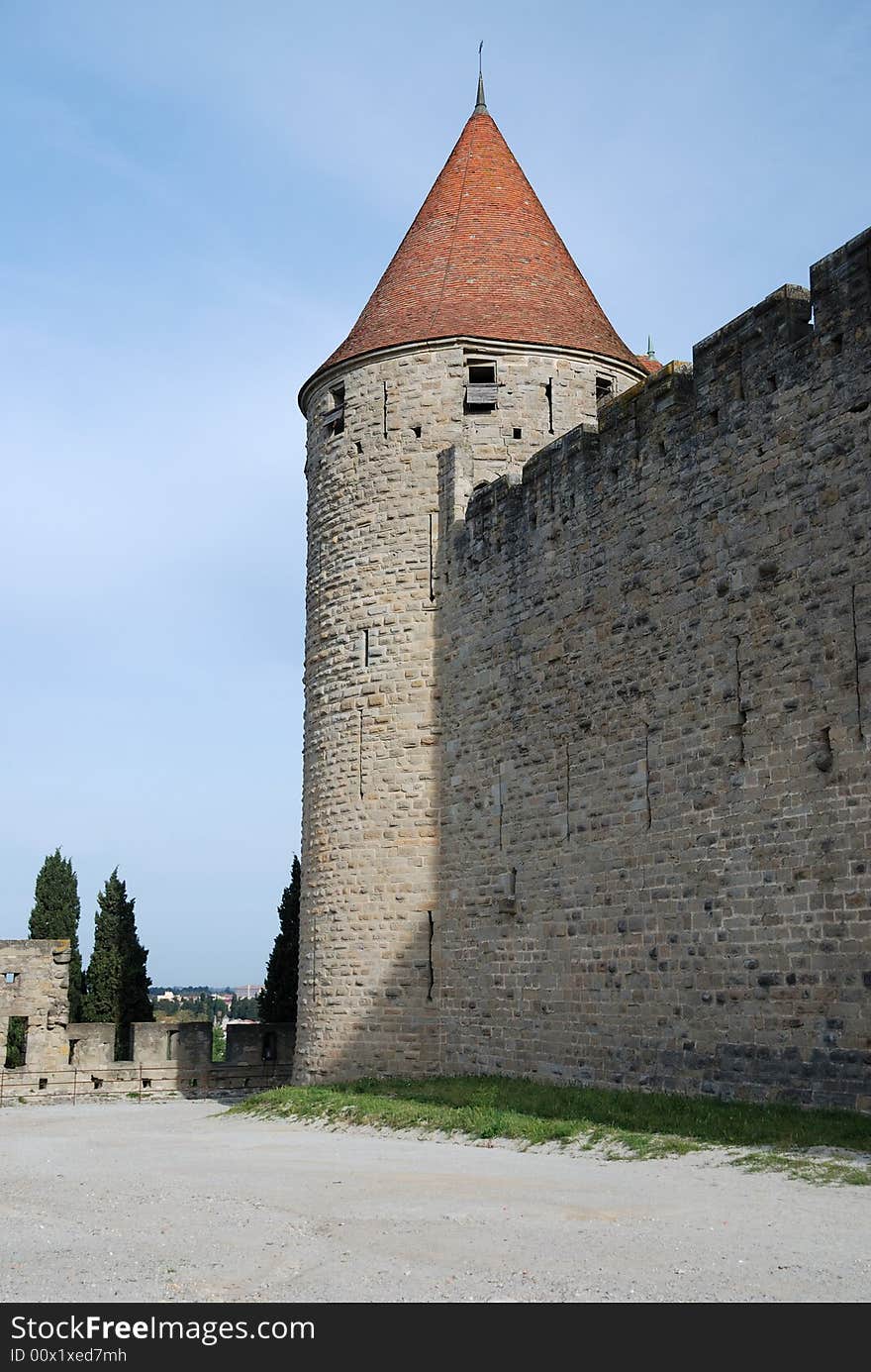 Old defense stone wall with loopholes and conic tower of Carcasson castle in sunlight against blue sky, France. Old defense stone wall with loopholes and conic tower of Carcasson castle in sunlight against blue sky, France