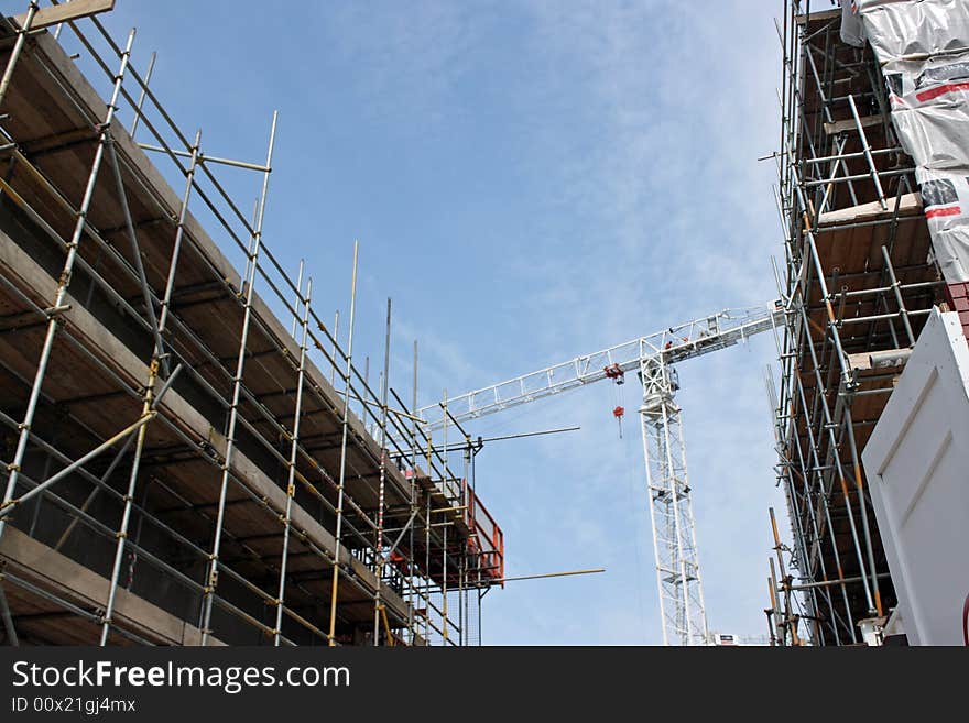 Construction crane against a blue sky with scaffold covered buildings both side. Construction crane against a blue sky with scaffold covered buildings both side