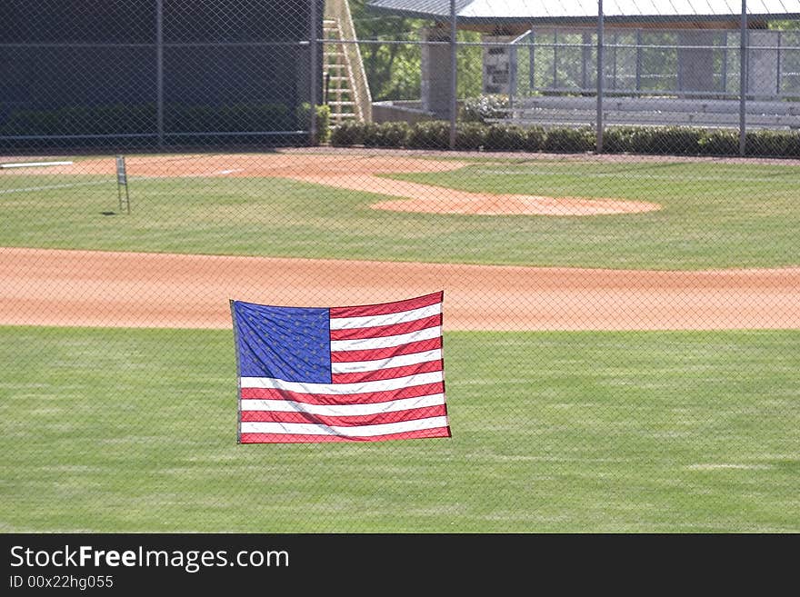 A view of a softball or baseball field from beyond the outfield fence with an American Flag. A view of a softball or baseball field from beyond the outfield fence with an American Flag