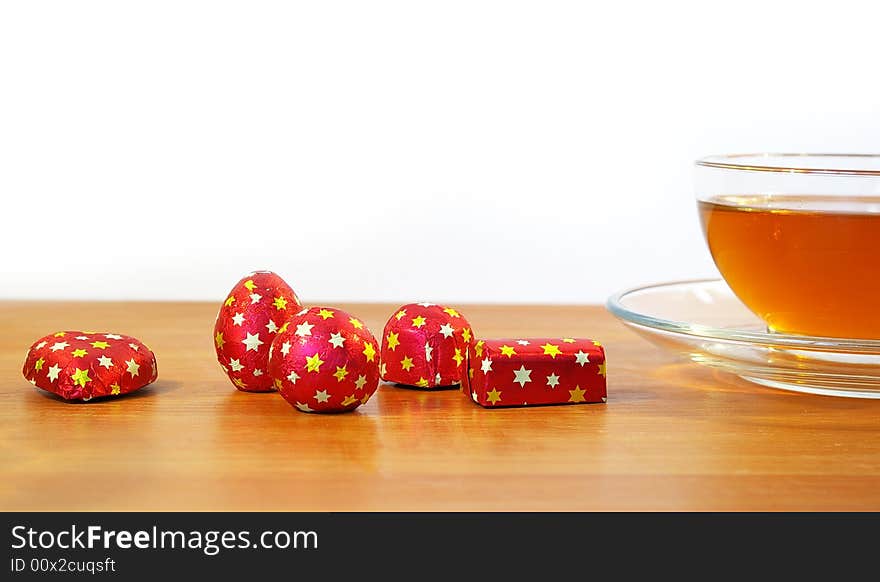 Chocolates in a red wrapper and a cup of tea. Chocolates in a red wrapper and a cup of tea