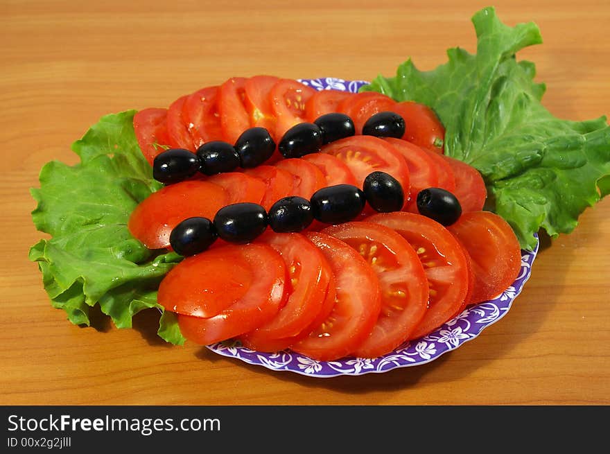 Tomatoes, leaves of salad and olives on a round plate. Tomatoes, leaves of salad and olives on a round plate