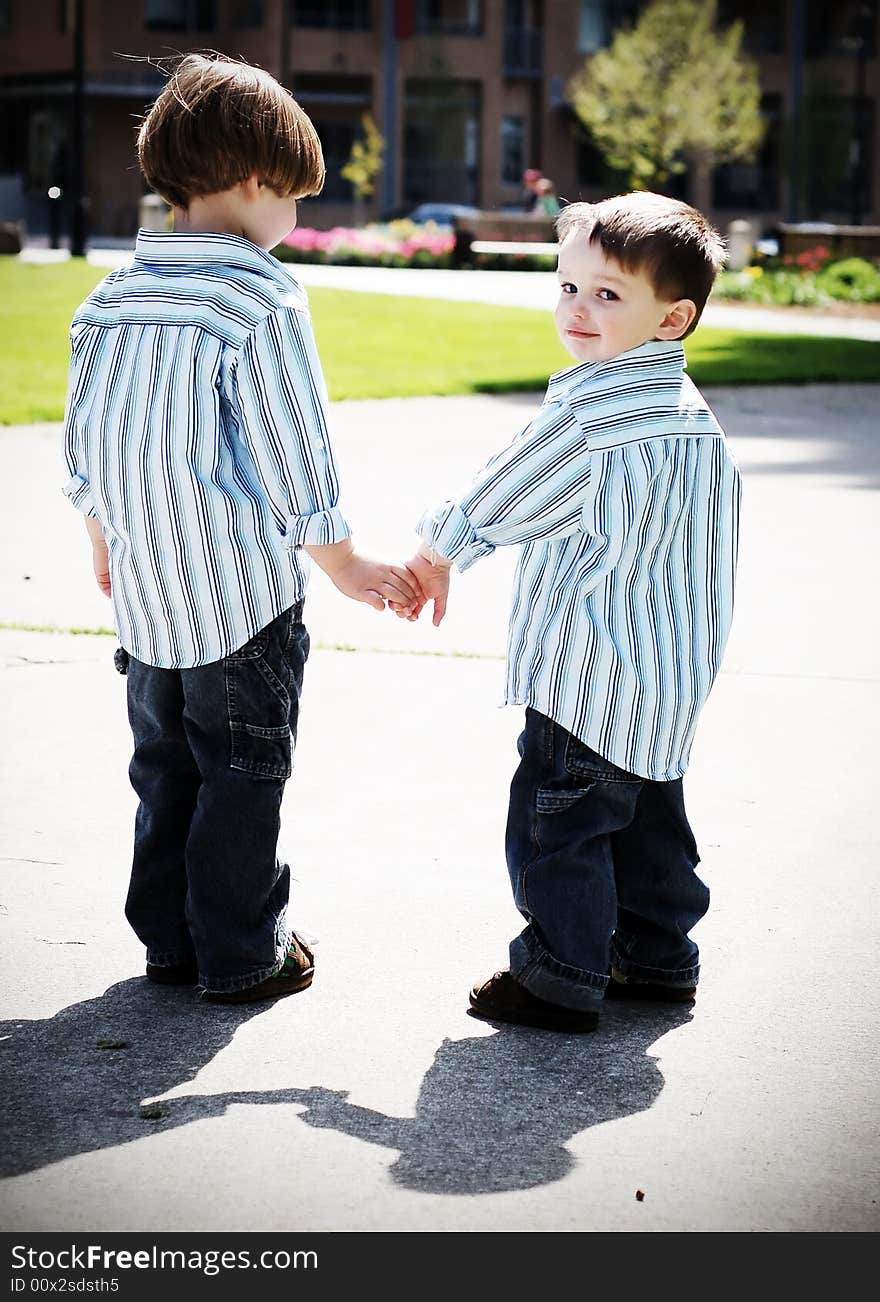 Two identically dressed brothers holding hands in a park. High-contrast style