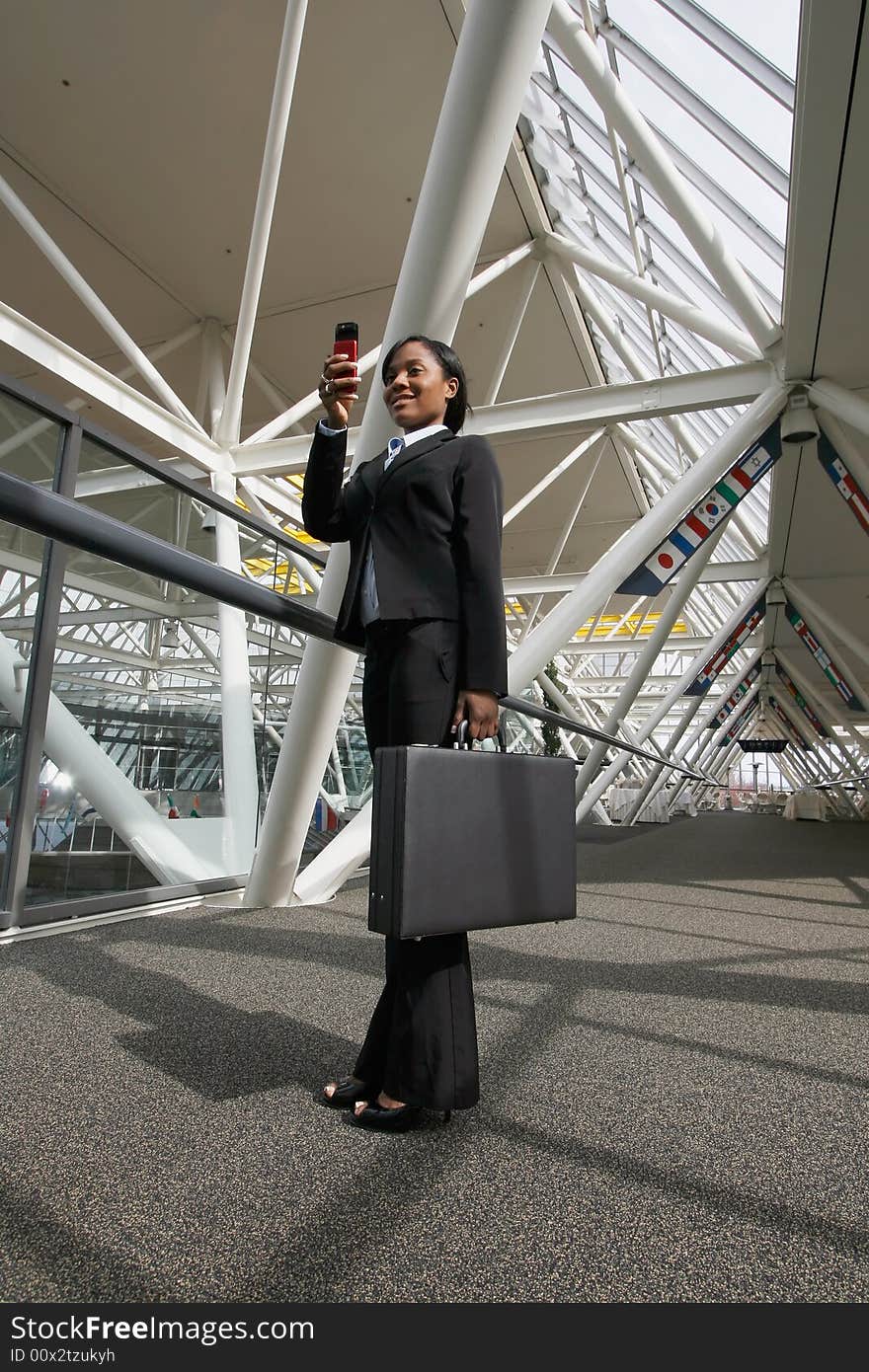 Businesswoman standing in an office atrium smiling as she takes a picture on her cellphone. Lobby has international flags adorning it. Vertically framed shot. Businesswoman standing in an office atrium smiling as she takes a picture on her cellphone. Lobby has international flags adorning it. Vertically framed shot.