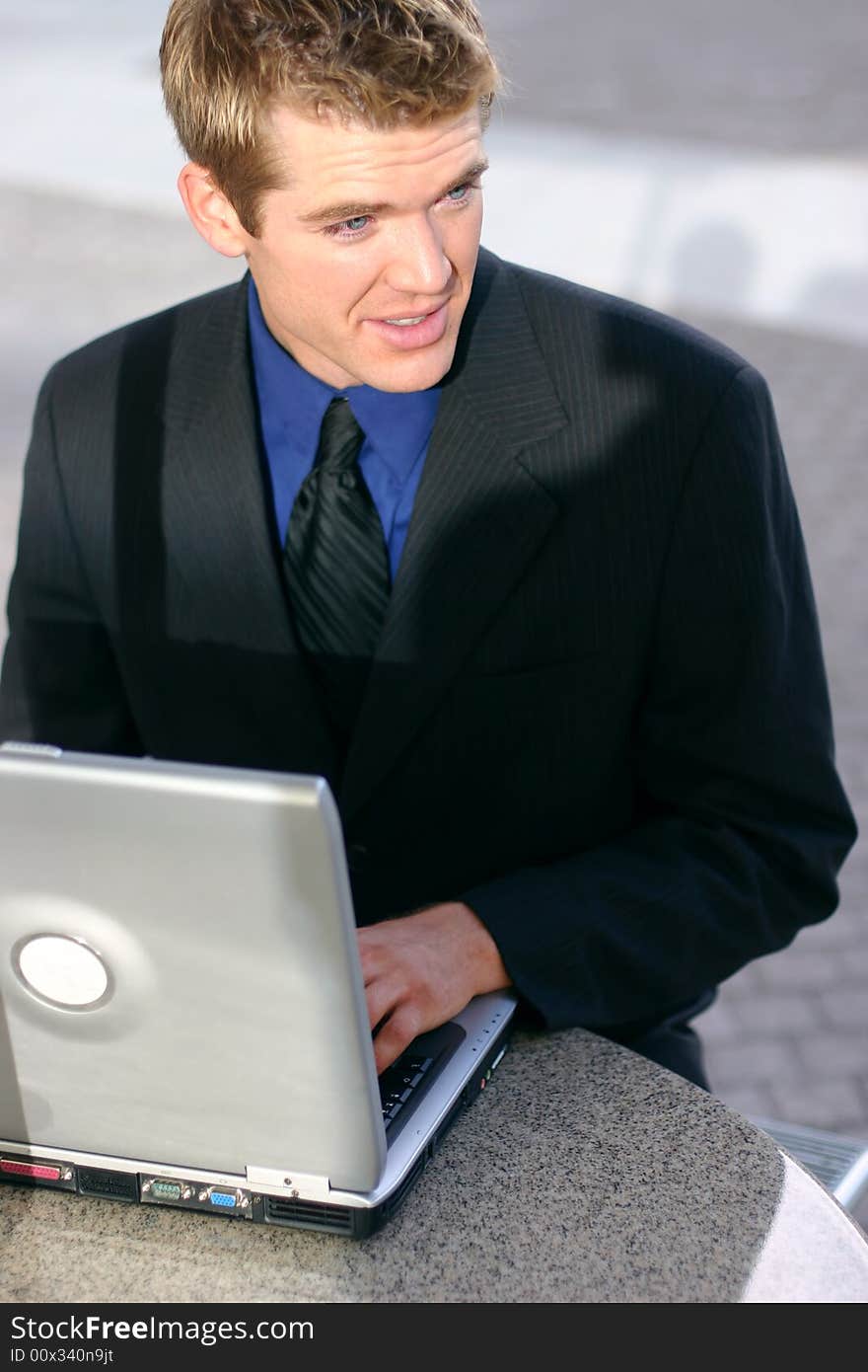 Businessman sitting down at table typing on laptop looking away. Businessman sitting down at table typing on laptop looking away