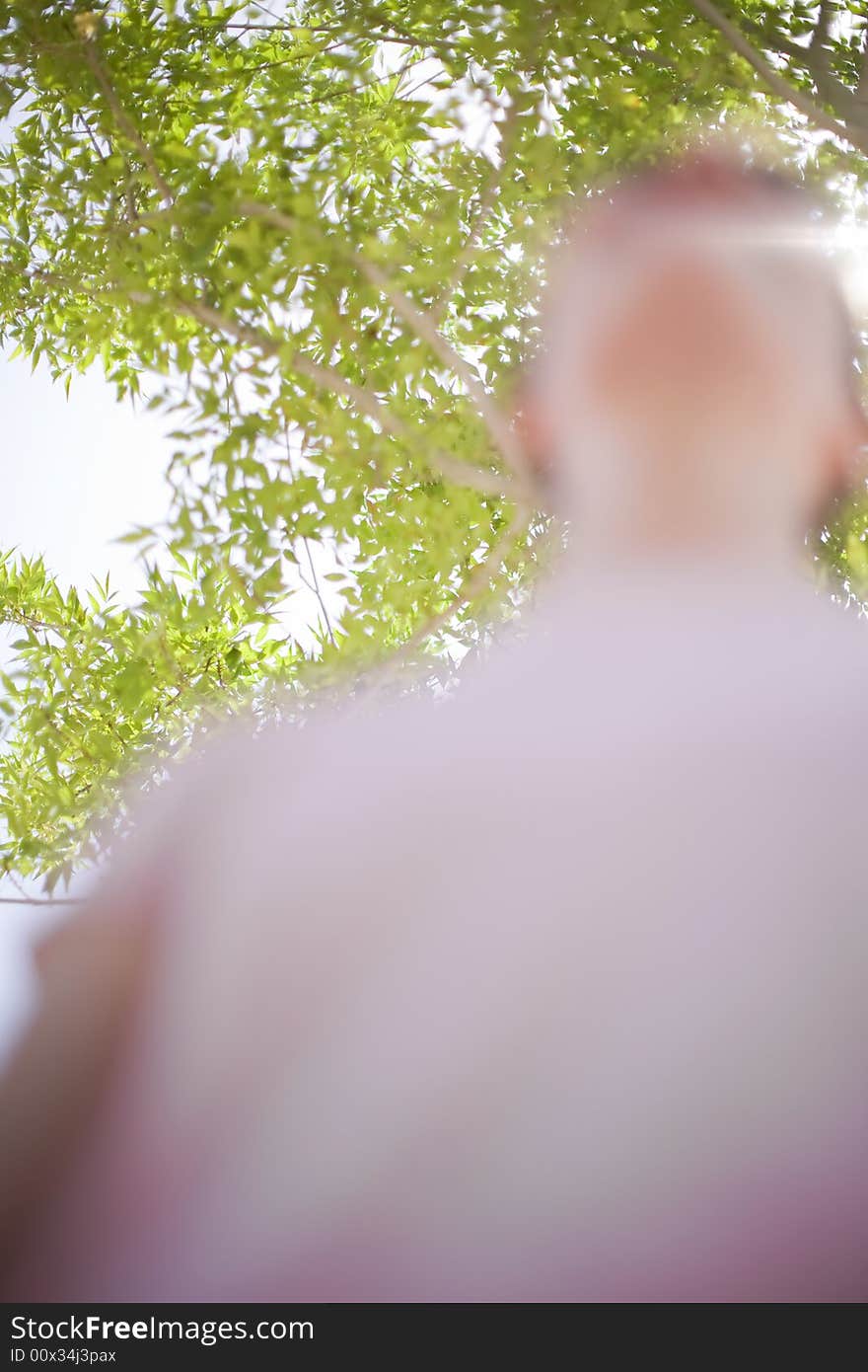 Blurred woman looking up standing underneath a green tree in the spring while the woman is wearing a pink t-shirt