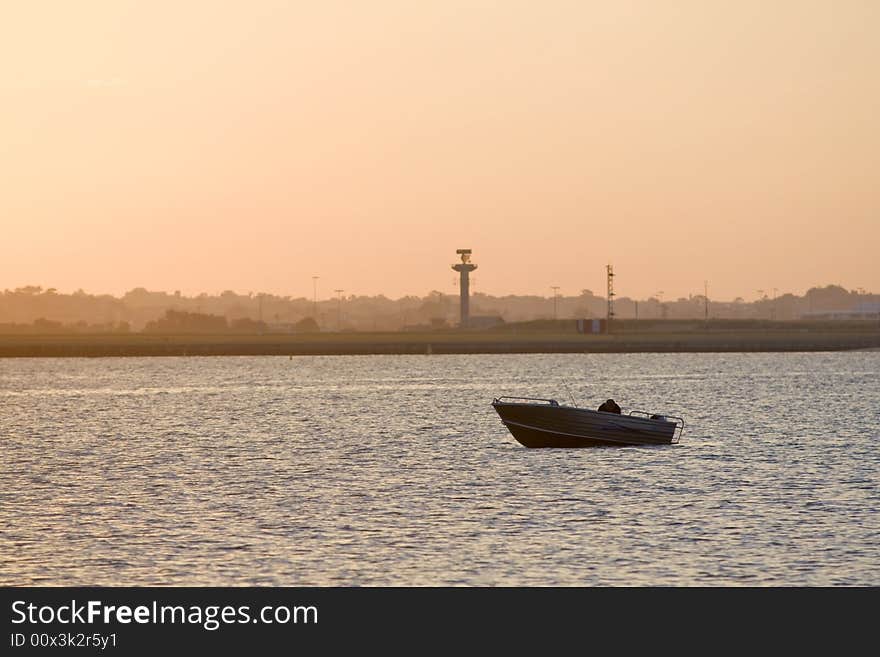 An angler enjoys a beautiful, golden, morning fishing from his small fishing boat on a sunlit sea. An angler enjoys a beautiful, golden, morning fishing from his small fishing boat on a sunlit sea.