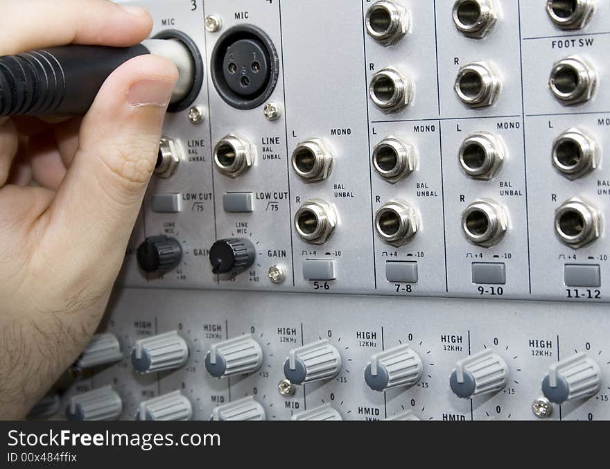 Close up of a hand plugging a mic on a soundboard. Focus on the hand. Close up of a hand plugging a mic on a soundboard. Focus on the hand.