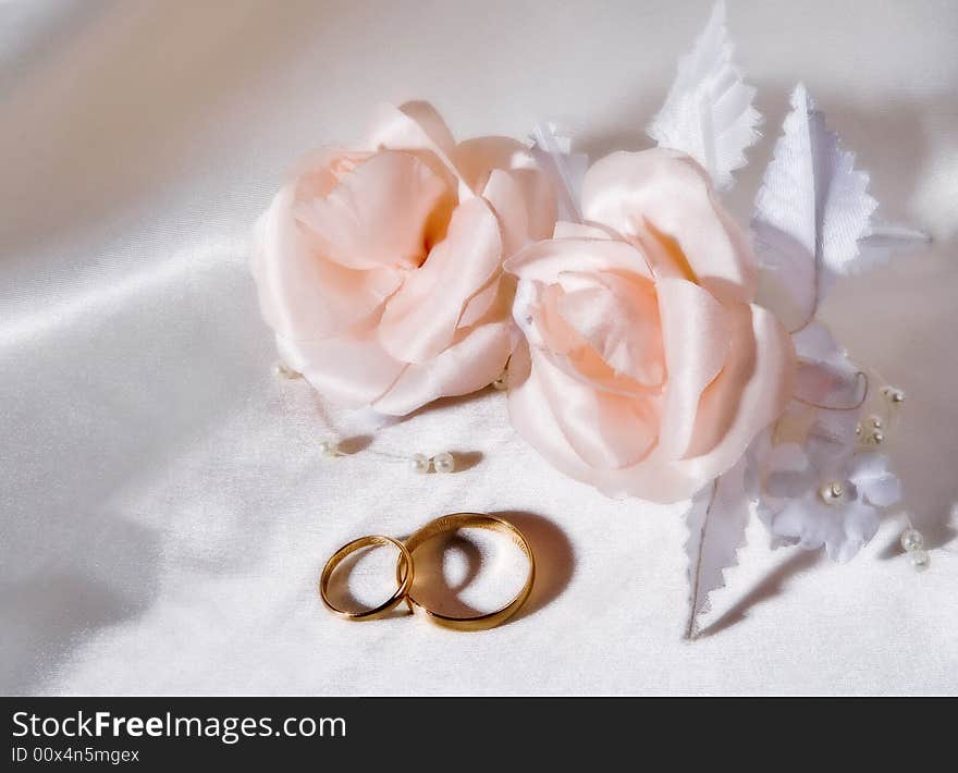 Wedding rings with artificial roses on white silk.