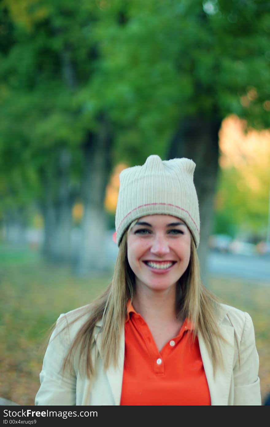 Young woman smiling outside in the fall with a cap and jacket on while wearing an orange shirt outside in a park. Young woman smiling outside in the fall with a cap and jacket on while wearing an orange shirt outside in a park