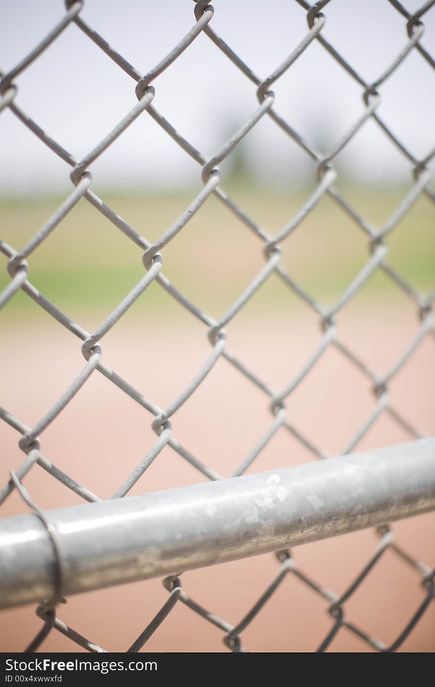Close-up of a baseball fence outside in the summer with a chain link fence in the front and a baseball field in the background. Close-up of a baseball fence outside in the summer with a chain link fence in the front and a baseball field in the background
