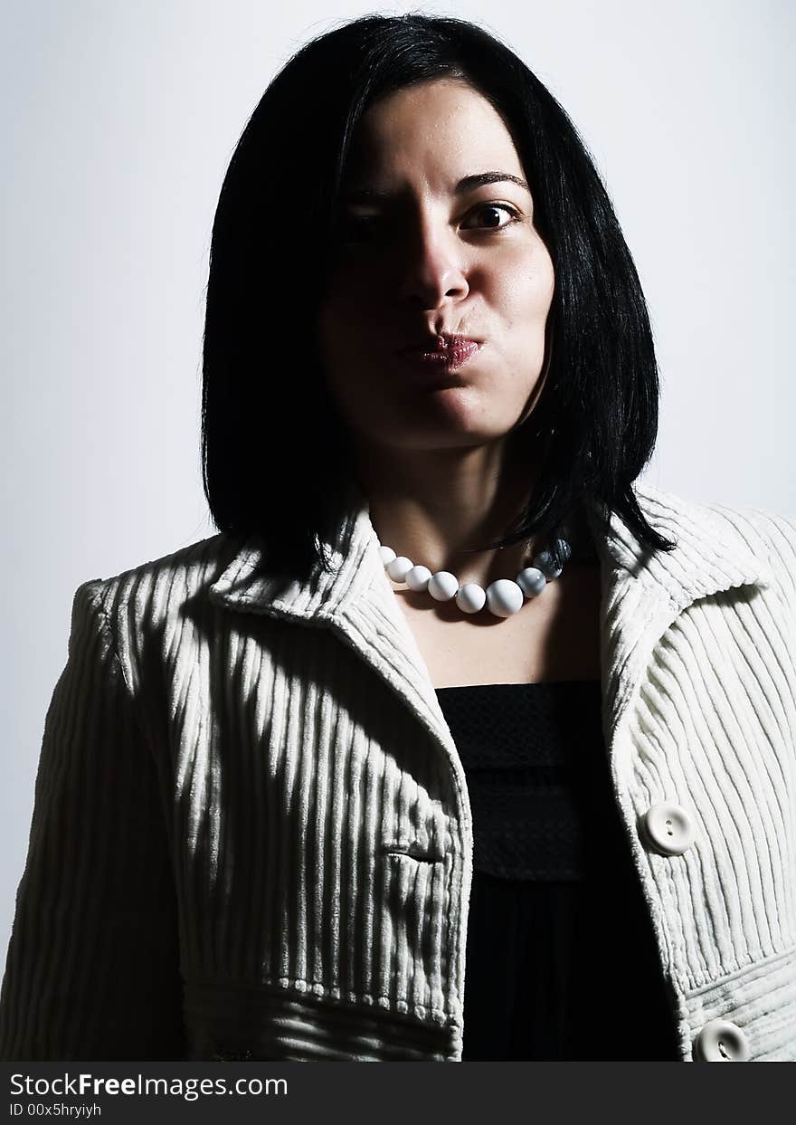 A high-key portrait about an attractive lady with black hair who is looking ahead, she is bulging out her cheeks and she is pouting. She is wearing a white coat, a black dress, and a white necklace. A high-key portrait about an attractive lady with black hair who is looking ahead, she is bulging out her cheeks and she is pouting. She is wearing a white coat, a black dress, and a white necklace.