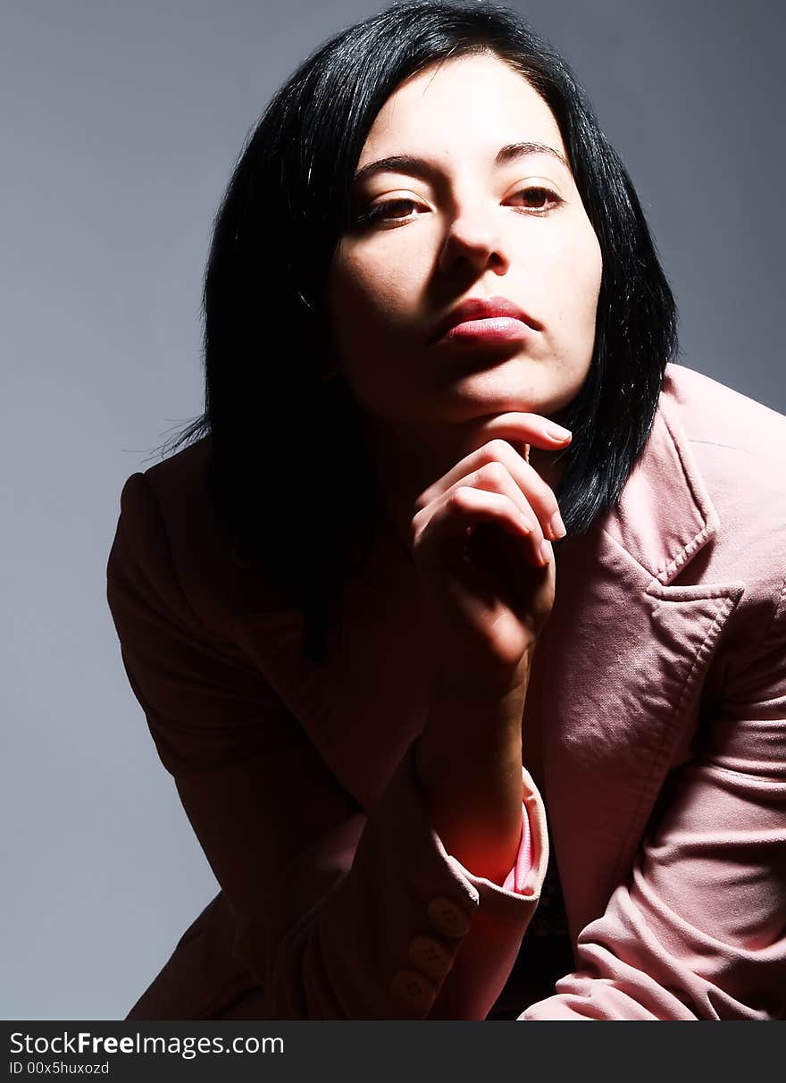 A high-key portrait about an attractive trendy girl with black hair who has a faraway look and she is thinking. She is wearing a stylish pink coat. A high-key portrait about an attractive trendy girl with black hair who has a faraway look and she is thinking. She is wearing a stylish pink coat.