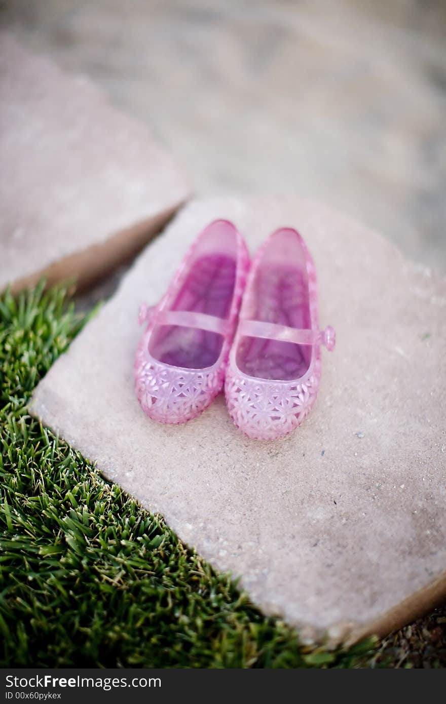 Little girl shoes that are pink sitting together on a brick wall next to grass outside in the spring