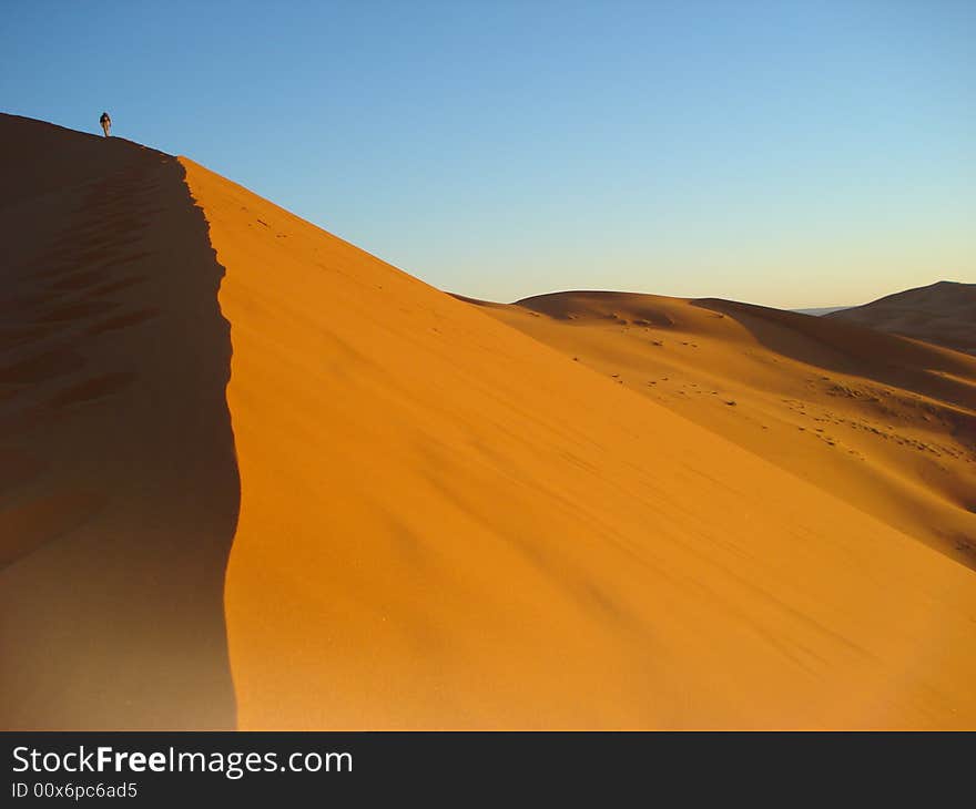 Climbing a large dune in the Sahara Desert during sunrise. Photo taken on the Eastern edge of Morocco. Climbing a large dune in the Sahara Desert during sunrise. Photo taken on the Eastern edge of Morocco.