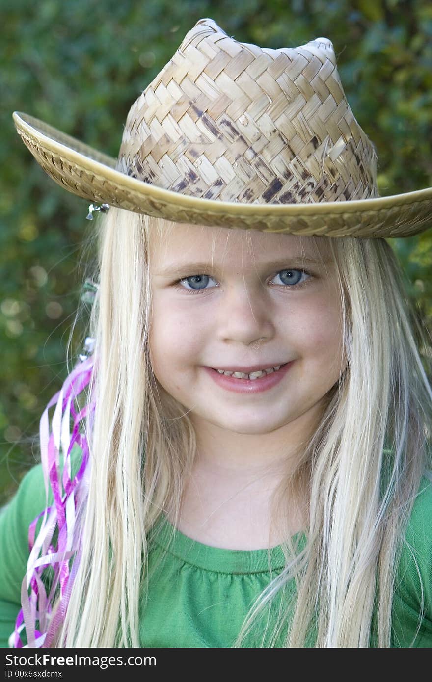 A little girl in a hat and green t-shirt with ribbons in her hair