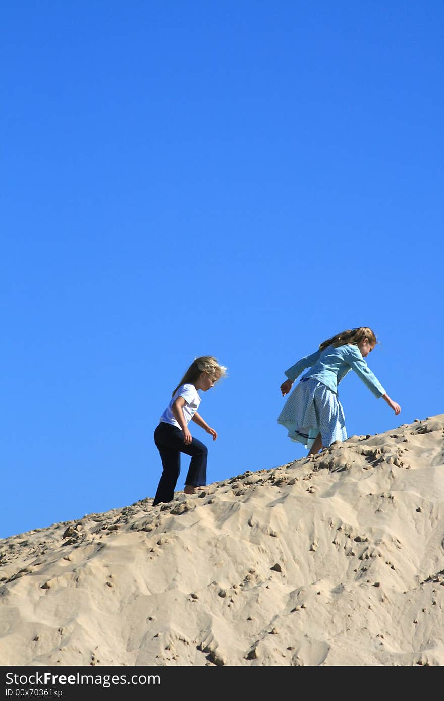 Two beautiful white caucasian girl children playing on a sand dune on the beach. Two beautiful white caucasian girl children playing on a sand dune on the beach