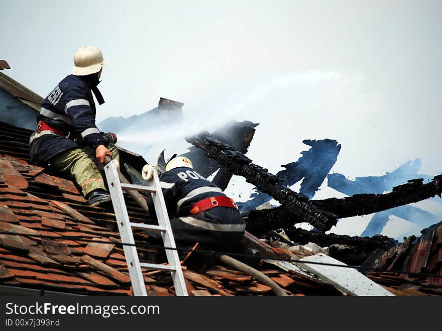 Two firemans in action on the roof of a burning house