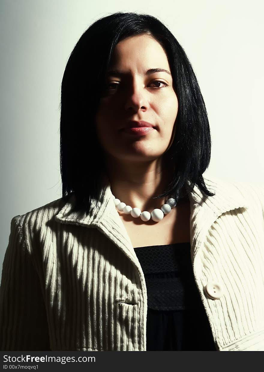 A high-key portrait about a happy attractive lady with black hair who is looking ahead and she has a charming look. She is wearing a white coat, a black dress, and a white necklace. A high-key portrait about a happy attractive lady with black hair who is looking ahead and she has a charming look. She is wearing a white coat, a black dress, and a white necklace.