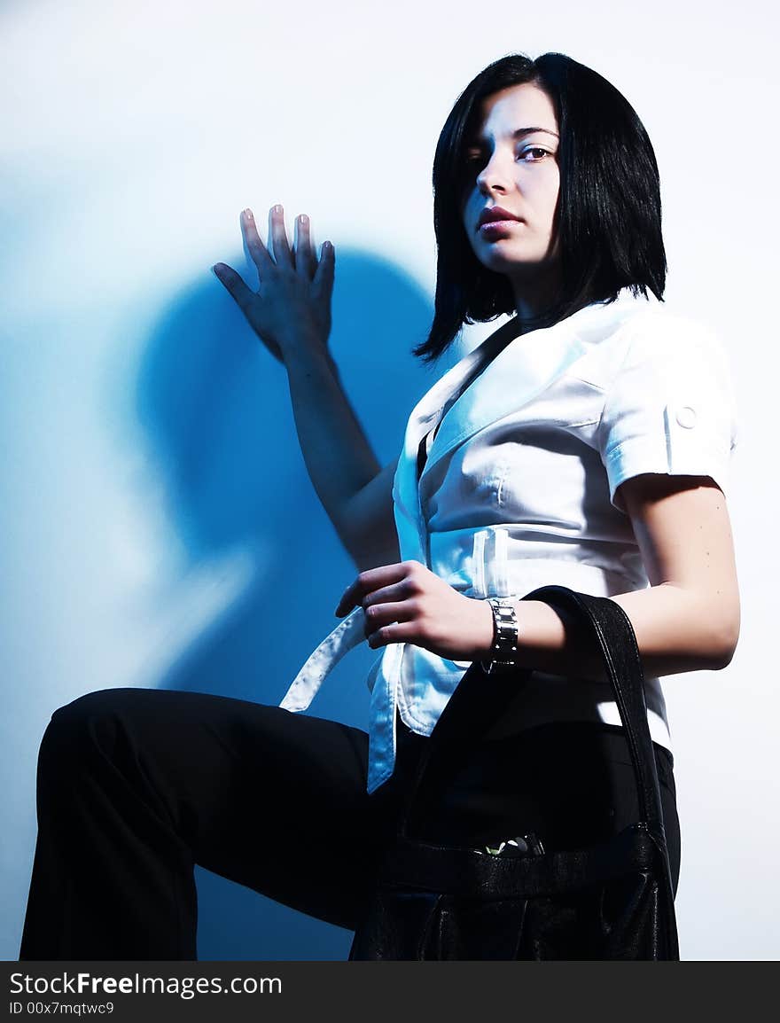 A high-key portrait about an attractive trendy lady with black hair who is leaning against the wall, she is lifting up her leg and she has a glamorous look. She is wearing black pants, a white coat and a stylish handbag. A high-key portrait about an attractive trendy lady with black hair who is leaning against the wall, she is lifting up her leg and she has a glamorous look. She is wearing black pants, a white coat and a stylish handbag.