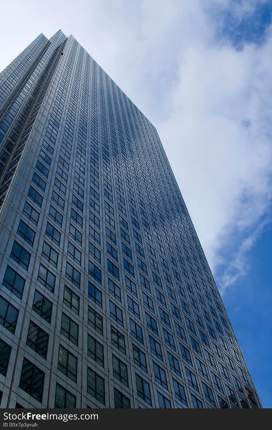 Looking up a very tall steel office building with cloudy sky