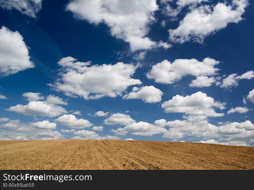 Blue sky with clouds over ploughed field.