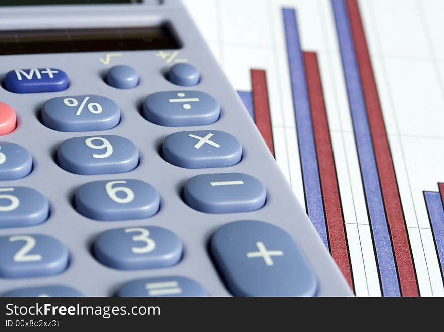 Close up of a blue calculator next to a red and blue bar chart on a white background. Close up of a blue calculator next to a red and blue bar chart on a white background