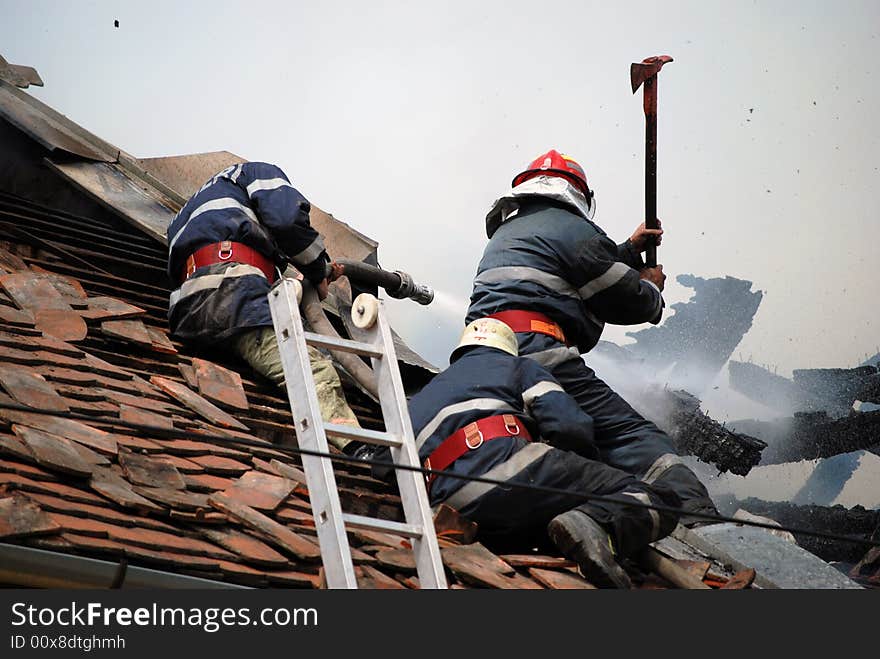 Three firemen in action on the roof of a burning house. Three firemen in action on the roof of a burning house