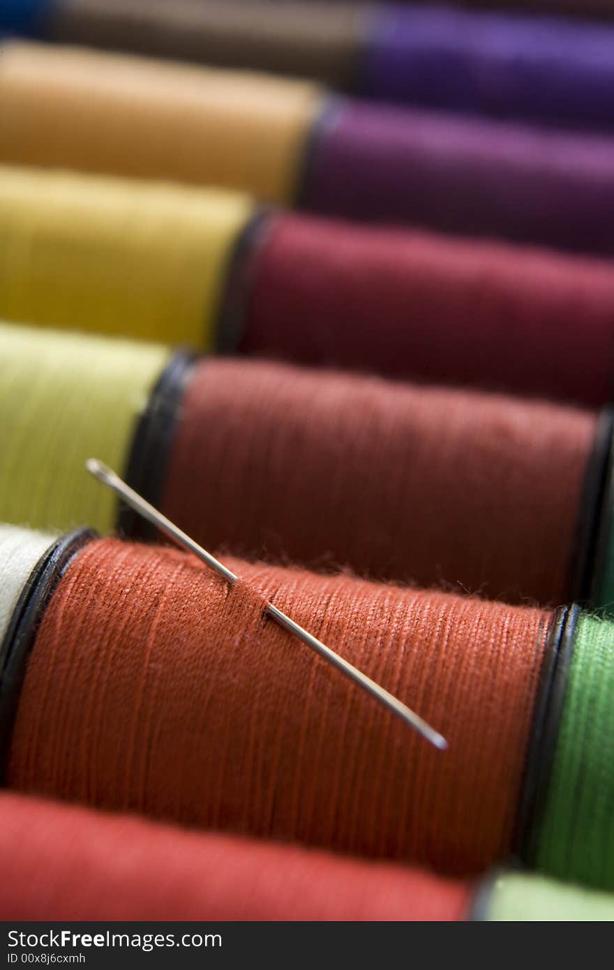 Various colours of cotton reelsin a row with a needle