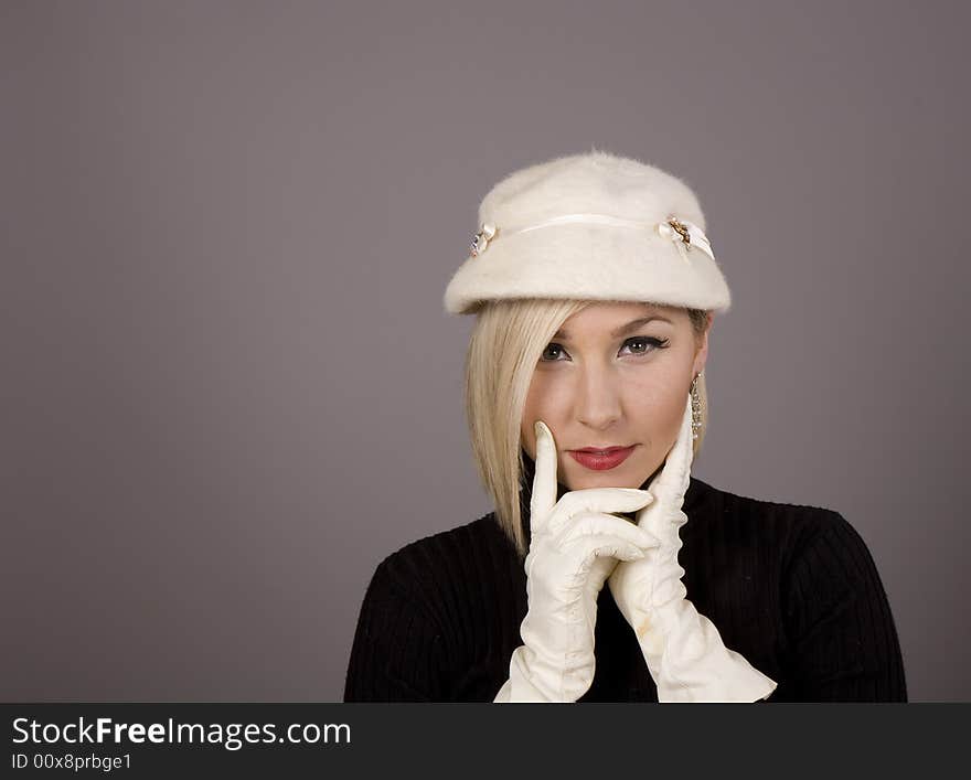 A blonde in a white fur hat and black turtleneck sweater with two white gloves. A blonde in a white fur hat and black turtleneck sweater with two white gloves