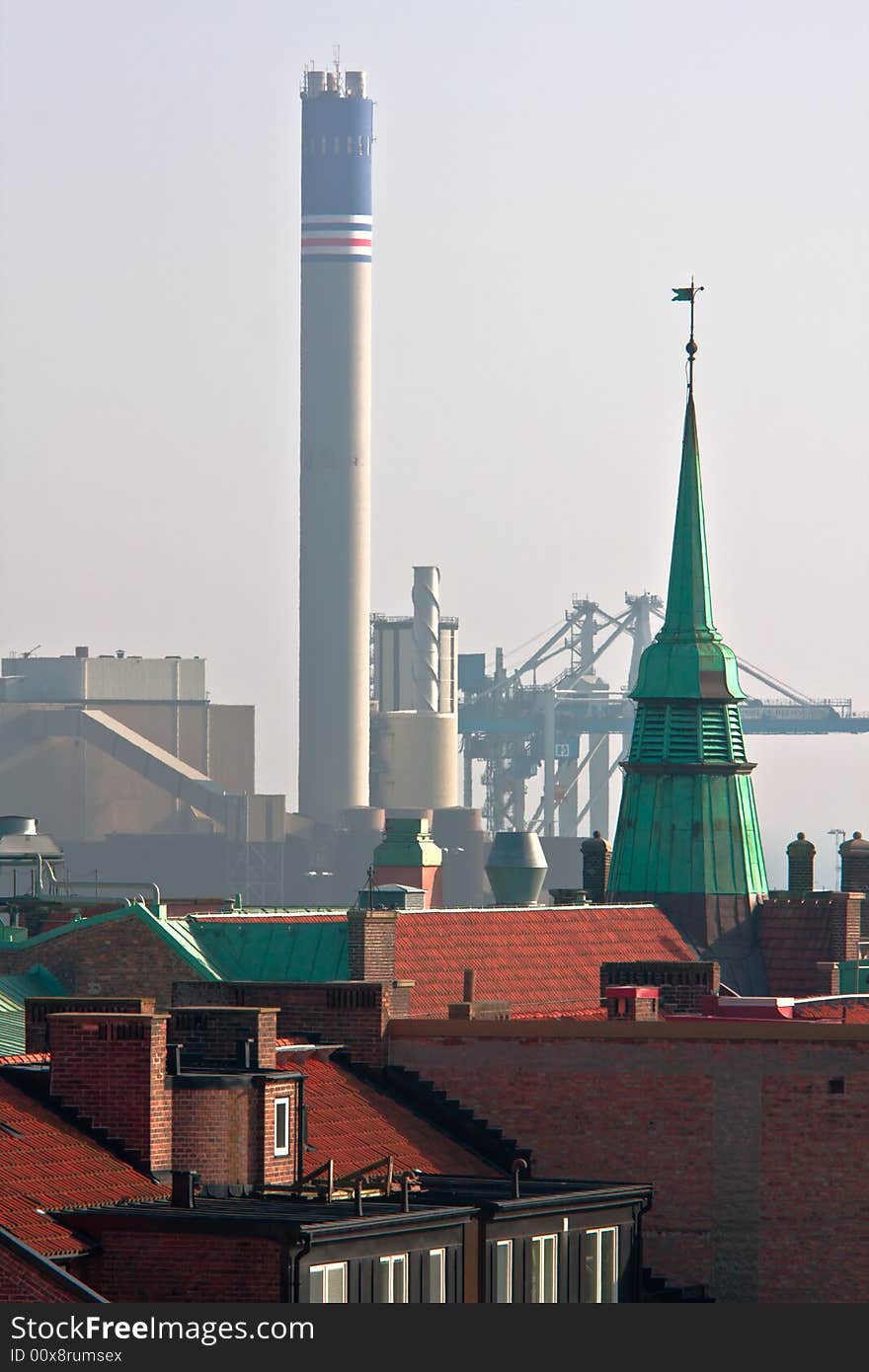 Contrast between urban rooftops and an industrial factory. Contrast between urban rooftops and an industrial factory