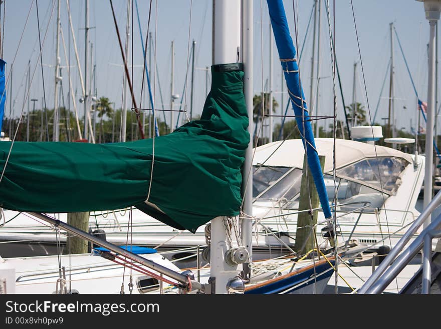 Sailboat Masts and Booms captures mast with a green sail cover as well as several poles lines and other nautical types of equipment and rigging in this marine background. Sailboat Masts and Booms captures mast with a green sail cover as well as several poles lines and other nautical types of equipment and rigging in this marine background.