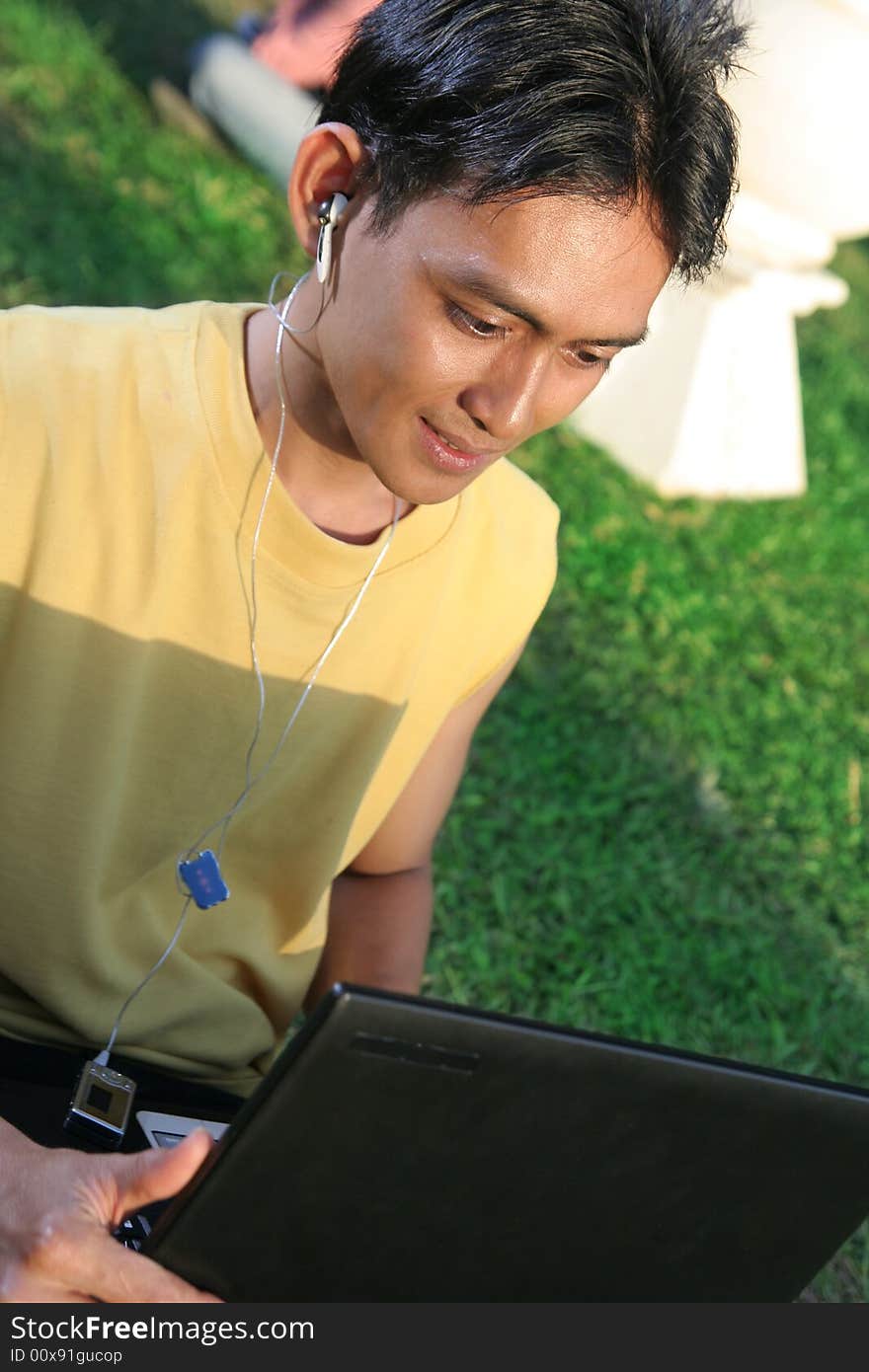 Young man with laptop and music on green grass. Young man with laptop and music on green grass