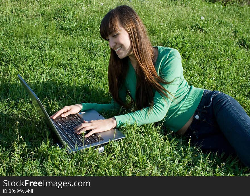 Happy young girl with laptop on meadow