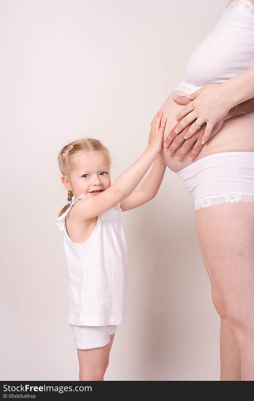 Daughter holding her mothers pregnant belly and watching in the camera. Daughter holding her mothers pregnant belly and watching in the camera