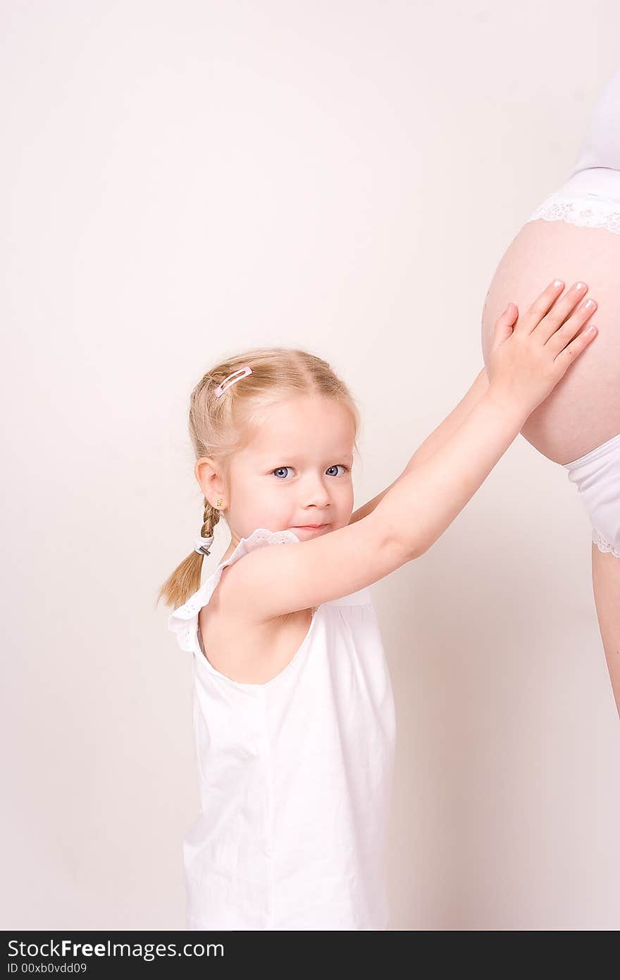 Daughter holding her mothers pregnant belly and watching in the camera. Daughter holding her mothers pregnant belly and watching in the camera