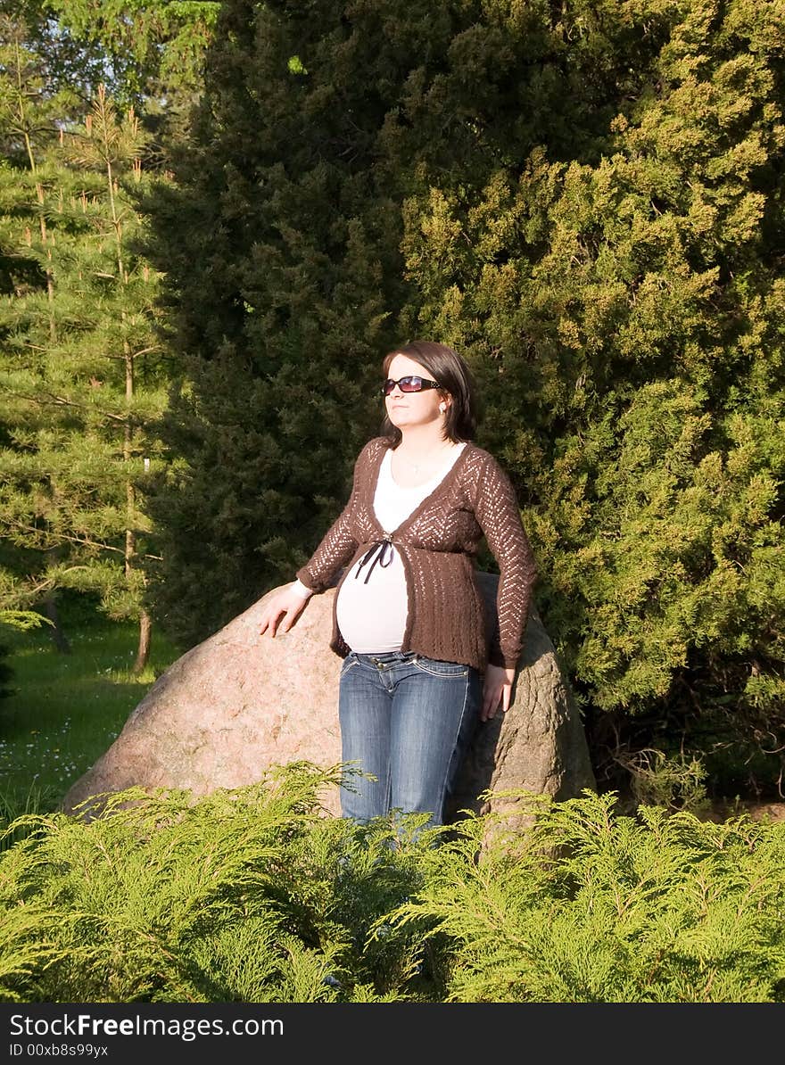 Pregnant woman taking sunbath while leaning against stone in the park. Pregnant woman taking sunbath while leaning against stone in the park