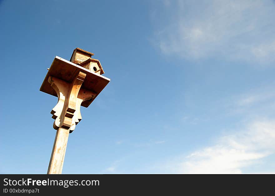 A wooden birdhouse on top of a pole with clouds in the background