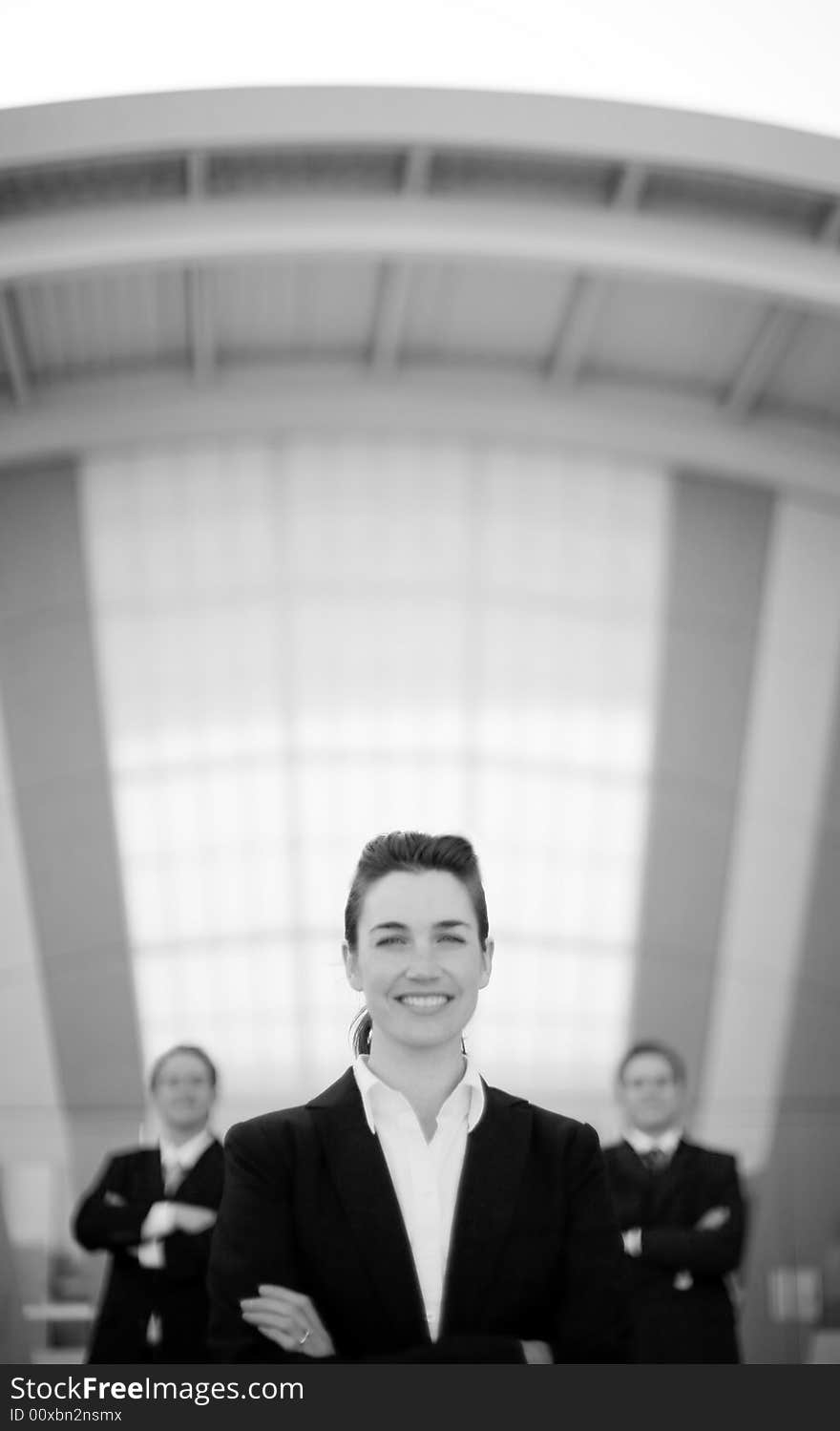 Businesswoman smiling standing in front of two businessmen with arms folded. Businesswoman smiling standing in front of two businessmen with arms folded