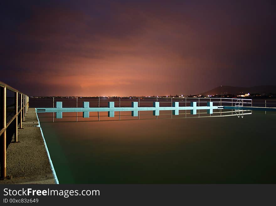 A swimming pool on a still evening, the overcast sky is lit up by southern steel producing factories creating a surreal effect. A swimming pool on a still evening, the overcast sky is lit up by southern steel producing factories creating a surreal effect