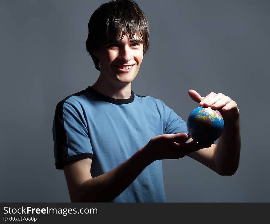 A portrait about a trendy attractive young man who is smiling, he is holding a globe in his hands and he is planning his trip. He is wearing a blue t-shirt. A portrait about a trendy attractive young man who is smiling, he is holding a globe in his hands and he is planning his trip. He is wearing a blue t-shirt.